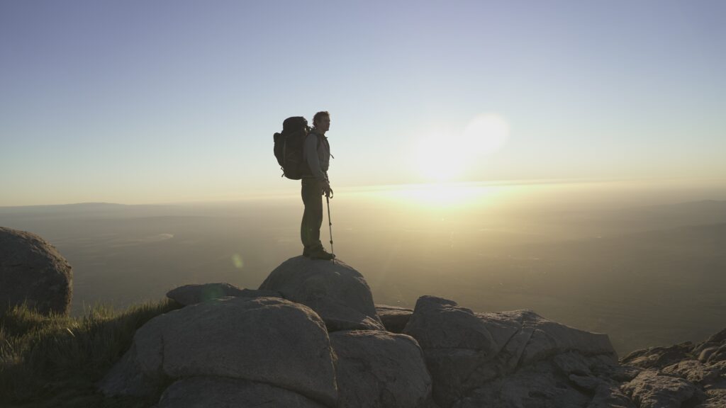 Un hombre en la cima de las sierras con vestimenta de trekking y el amanecer de fondo